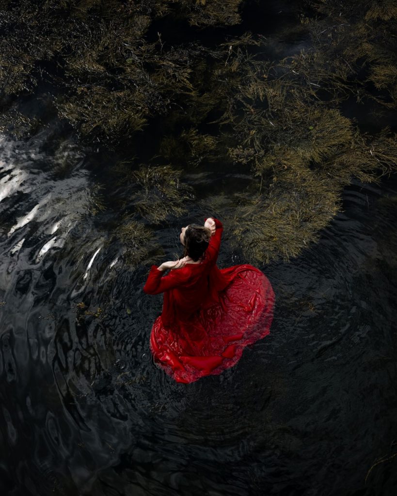 Cig Harvey photograph of woman in red dress by water and greenery