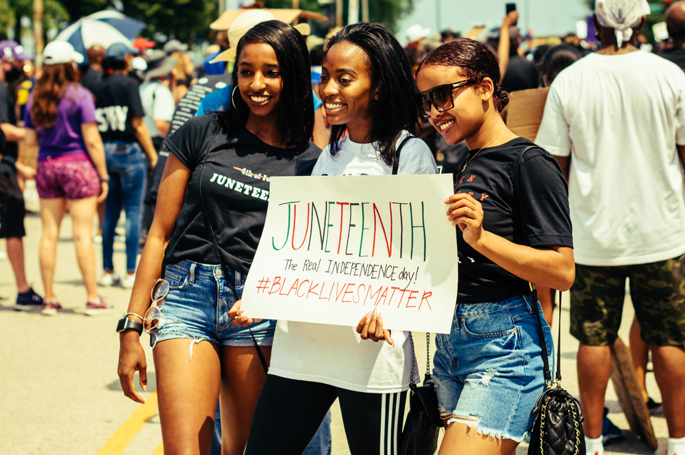 three Black women hold Juneteenth poster