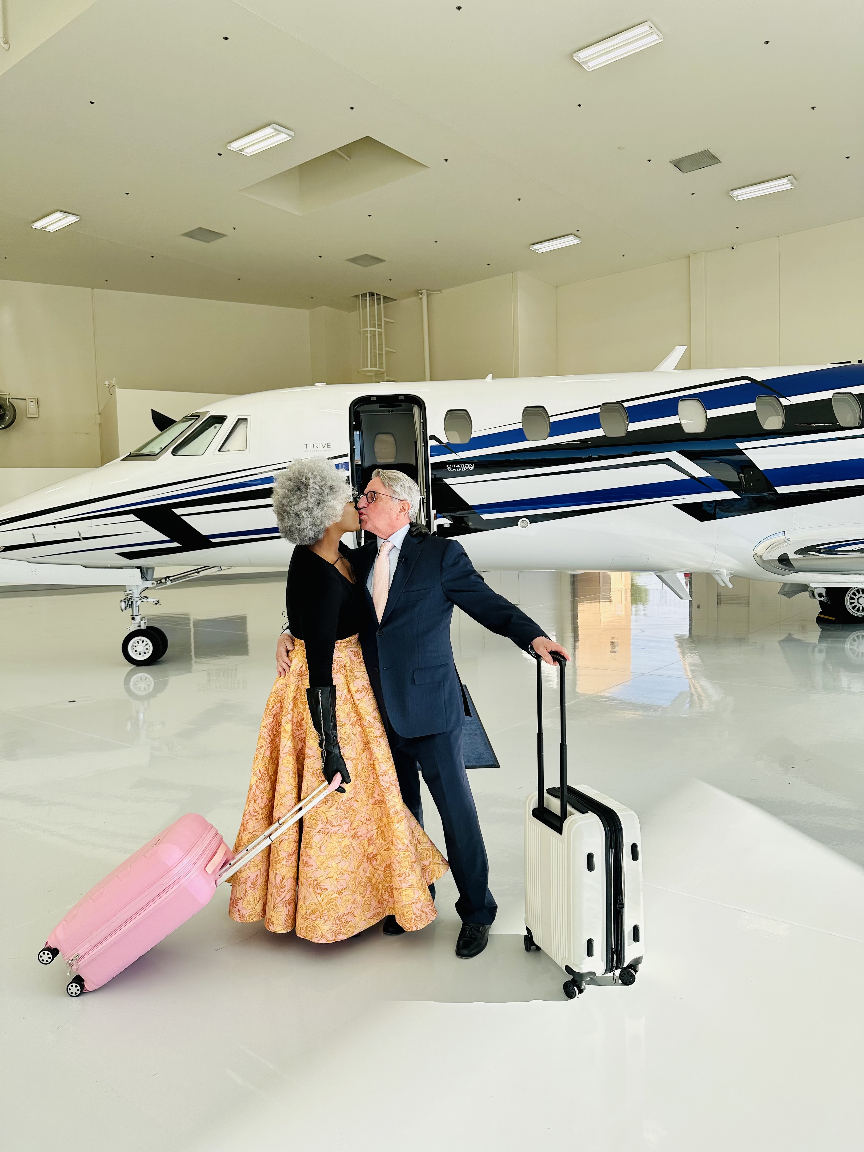 Couple kissing with luggage in middle of Thrive Aviation Private Jet Hangar